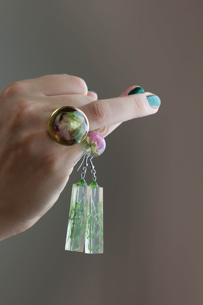 Artistic close-up of a woman's hand showcasing handmade resin jewelry with floral design.