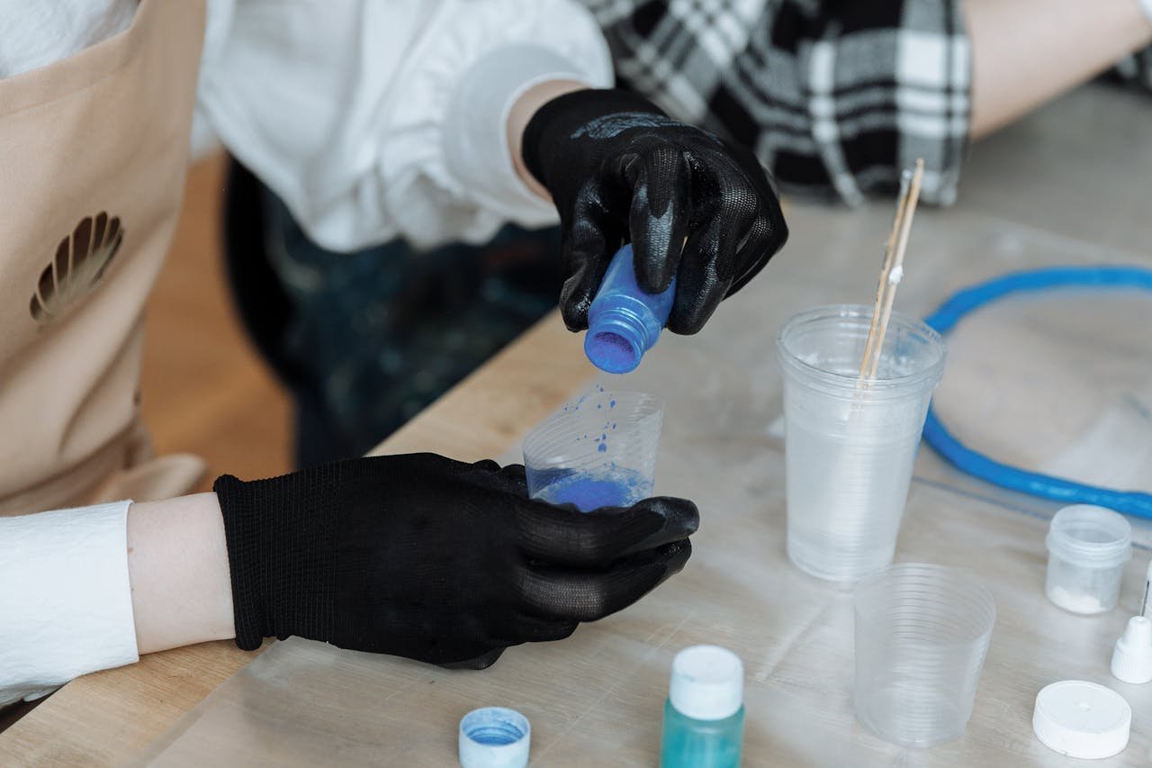 Close-up shot of gloved hands mixing colored pigments in plastic cups for art creation.